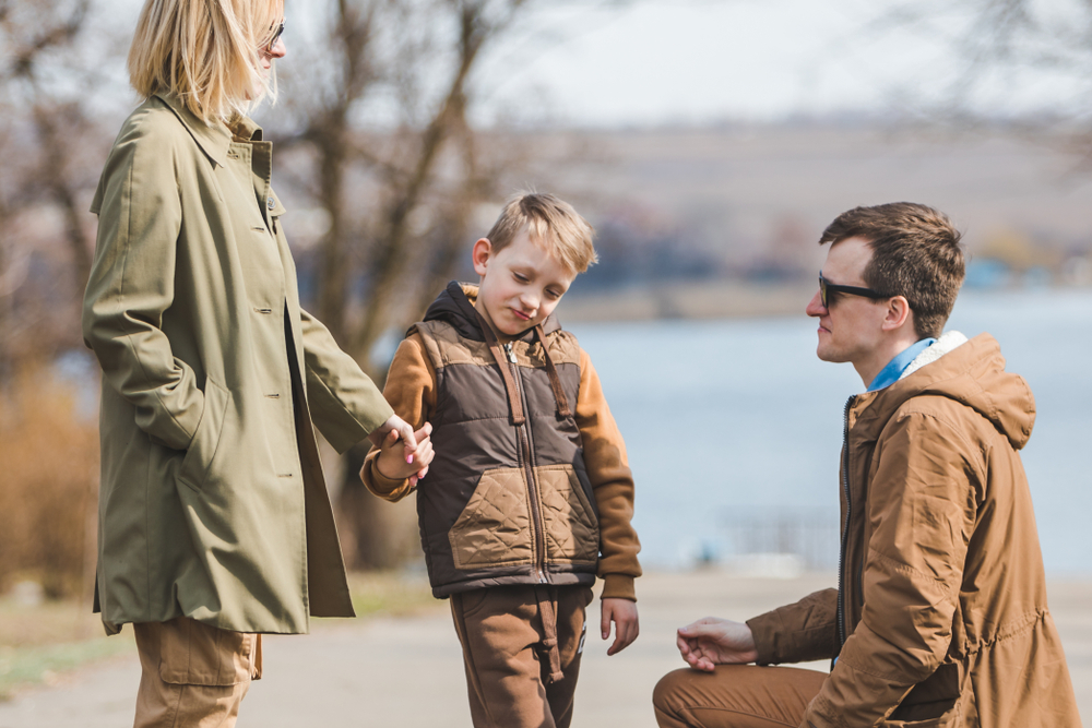 Mother holding child's hand and father kneeling beside him in a park